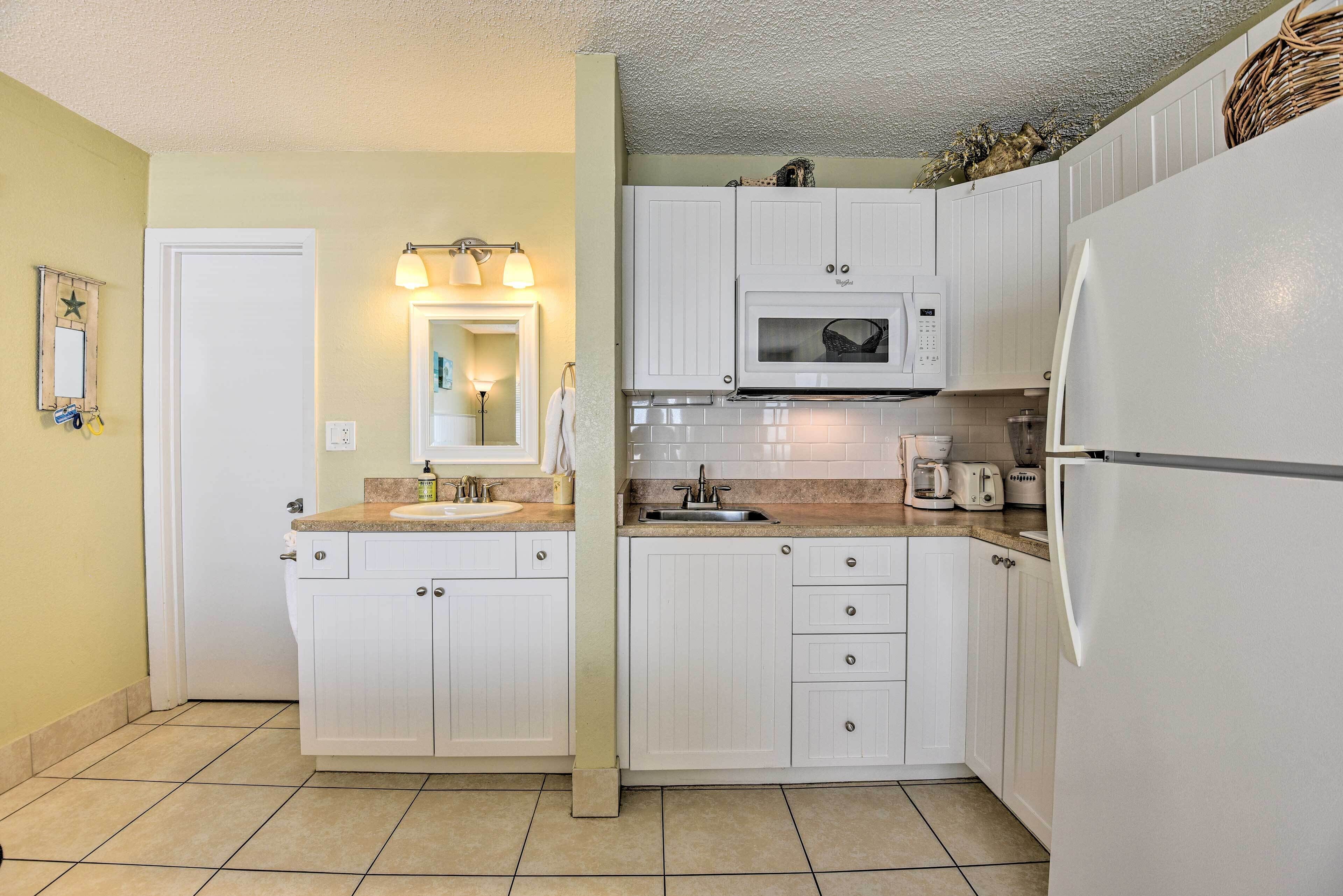 A compact kitchen with white cabinetry, a microwave, a refrigerator, and a sink.