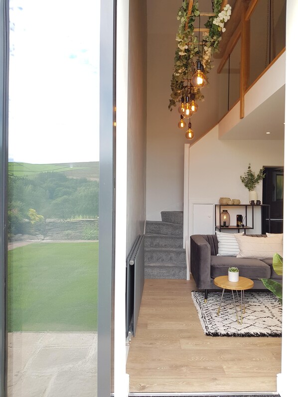 A modern living room with a grey sofa, a round coffee table, and a view of a green landscape through a large window.