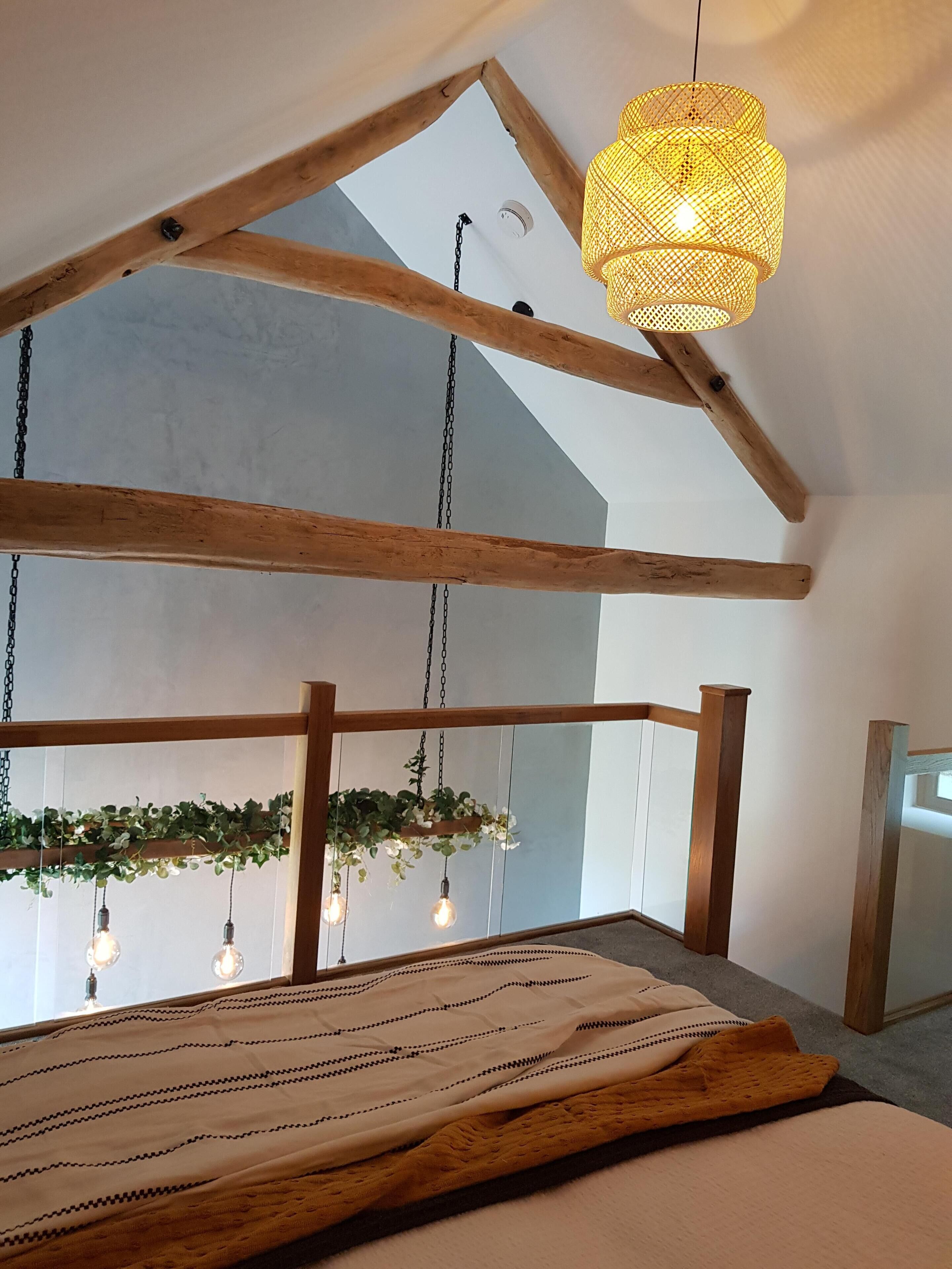 A room with a sloped ceiling, wooden beams, hanging light fixtures, and a bed with a patterned bedspread.