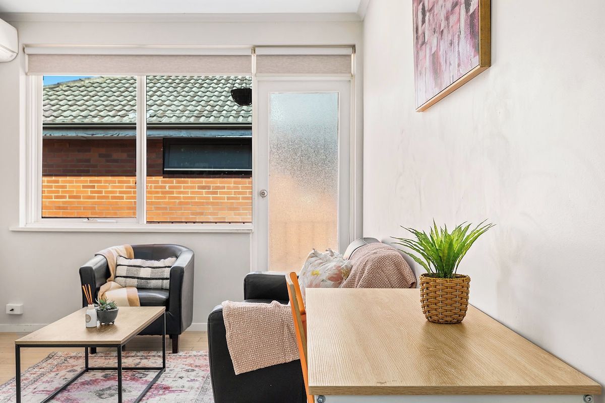 A compact living space with a single sofa, a small table, a potted plant, and a window with a view of a brick building.