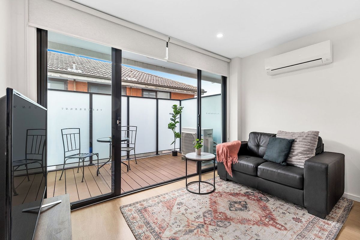 A modern living room with a sofa, a coffee table, and a view of an outdoor balcony.