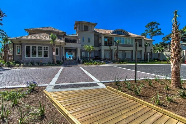 A two-story house with a driveway leading to a gated entrance, surrounded by landscaped areas and palm trees.