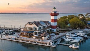 Une propriété située au bord de l’eau, comprenant un phare, un quai avec des bateaux et un bâtiment doté d’une grande fenêtre donnant sur l’eau.