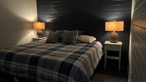 Un dormitorio con cabecera de madera oscura, colcha escocesa, dos lámparas de noche y una mesita de noche de madera.