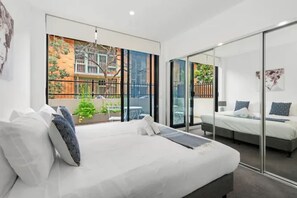A modern bedroom with a large bed, a glass partition, and a view of a cityscape.