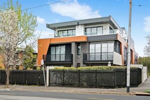 A modern two-story building with a flat roof, large windows, and a black metal fence.