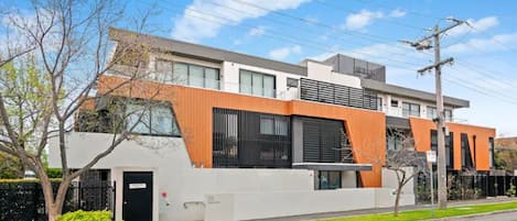 A modern two-story building with a flat roof, large windows, and a combination of white and orange facade.