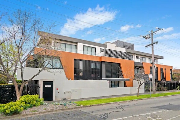 A modern two-story building with a flat roof, large windows, and a combination of white and orange facade.