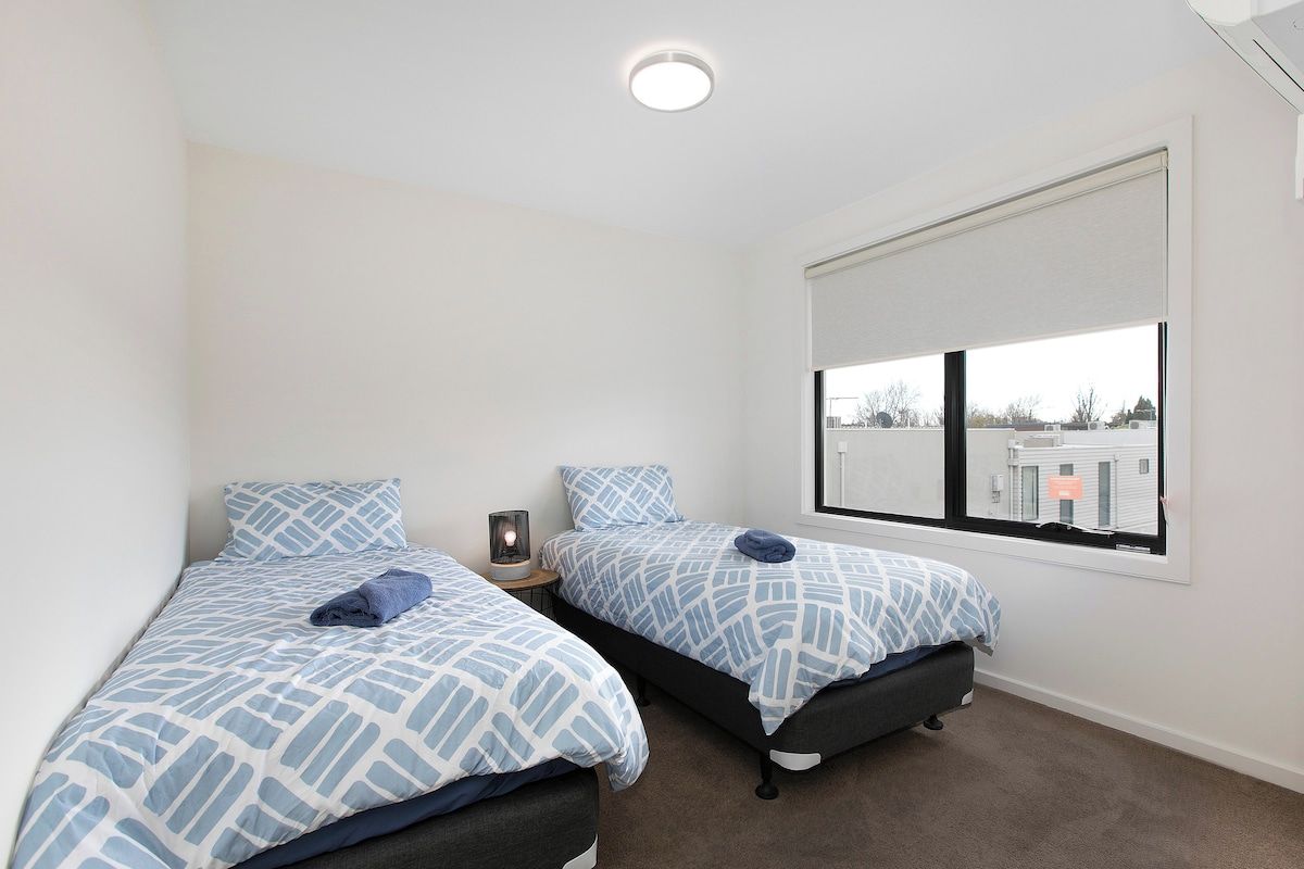 A bedroom with two beds, a window with a view, and a ceiling light.