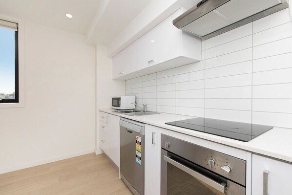 Una cocina moderna con armarios blancos, microondas, lavavajillas y horno empotrado.