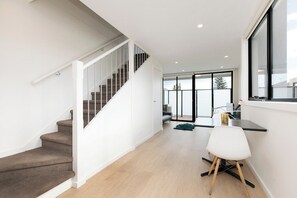 A modern interior with a staircase, a dining area, and a view through large windows.