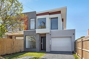 A modern two-story house with a garage, a front yard, and a wooden fence. - Domi Rentals - The Rayhur Residence (Clayton South)