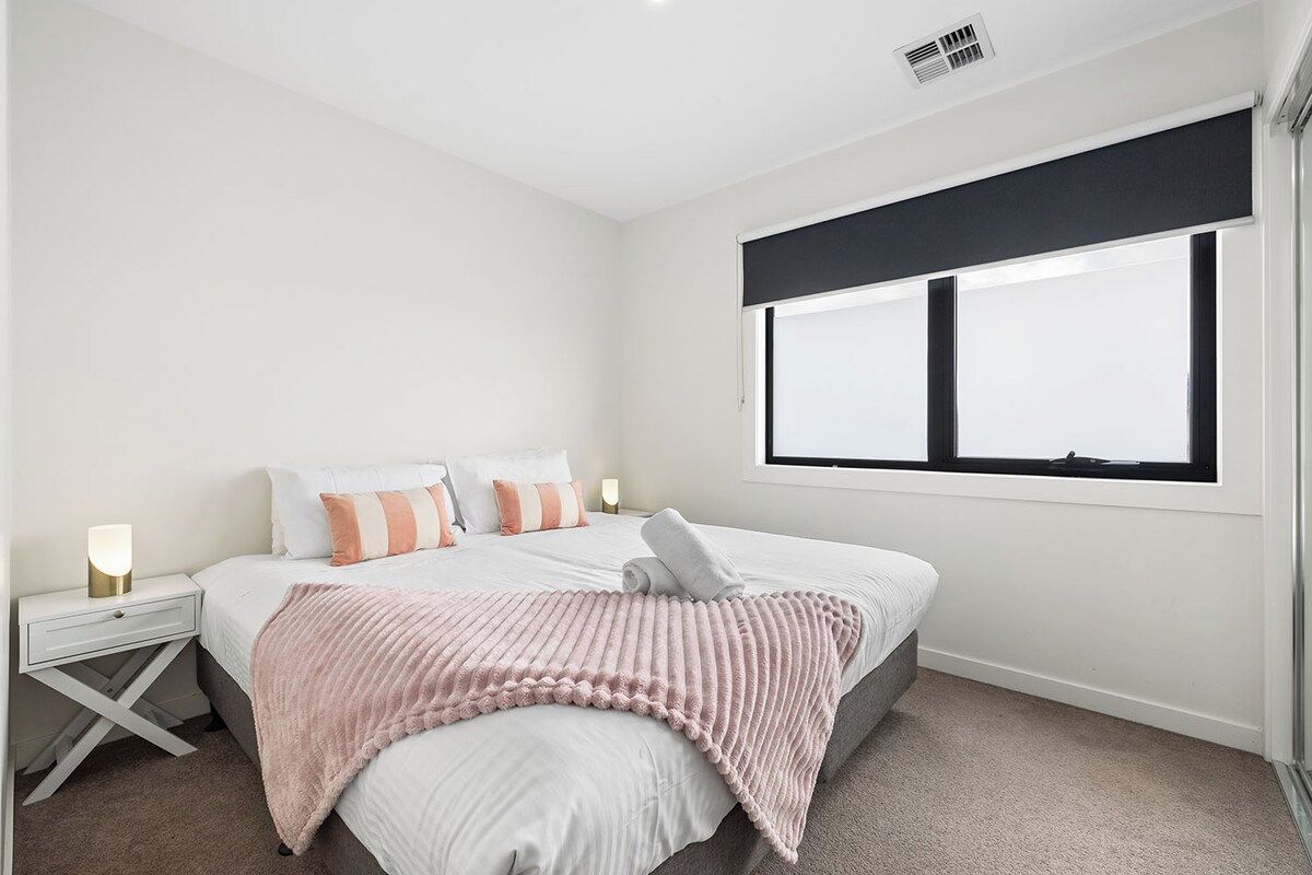 A bedroom with a bed, bedside tables, a window, and a wall-mounted air vent.