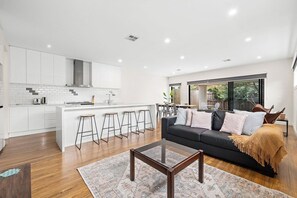 A modern kitchen with white cabinetry, a central island, and bar stools. - Domi Rentals - The Rayhur Residence (Clayton South)