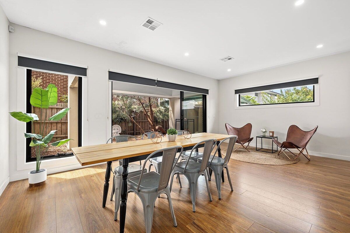 A dining area with a wooden table and metal chairs, a small rug, and a window with a view of greenery.