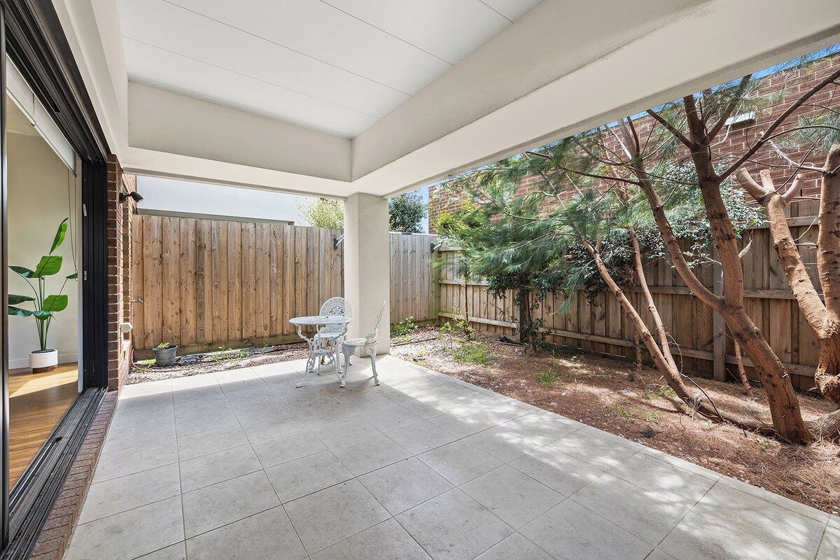 A covered patio with a tiled floor, a wooden fence, and a tree.
