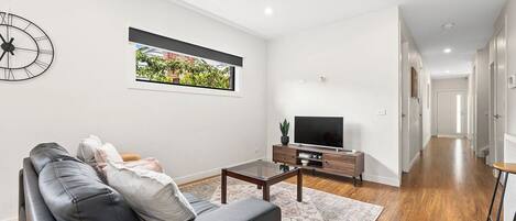 A modern living room with a sofa, a coffee table, a flat-screen TV, and a wall-mounted clock.