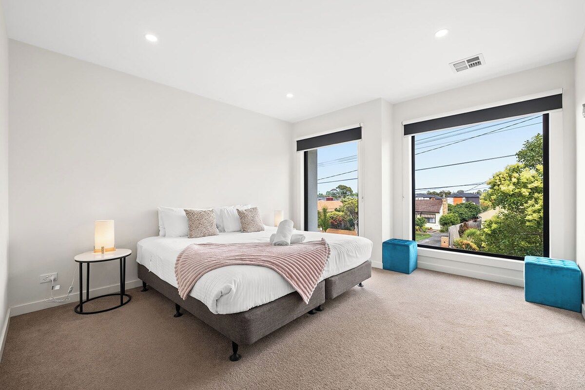A bedroom with a bed, bedside table, and large windows.