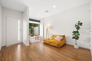 Una habitación con piso de madera, un sofá con cojines, una planta en maceta y una lámpara.