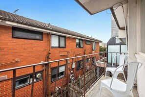 A residential building with a brick facade, multiple windows, and a balcony with a white chair.