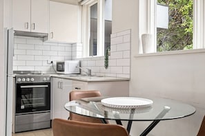 A modern kitchen with white cabinetry, a stainless steel oven, a microwave, and a glass table with chairs.