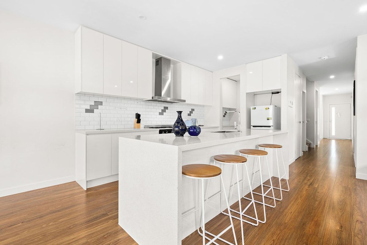 A modern kitchen with white cabinetry, a central island with stools, and a stainless steel range hood.