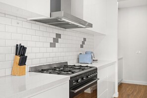 A modern kitchen with white tiles, a gas stove, and a stainless steel range hood.