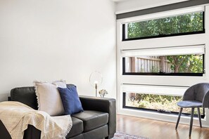 A modern living room with a black leather sofa, a grey armchair, and a large window with multiple panes.