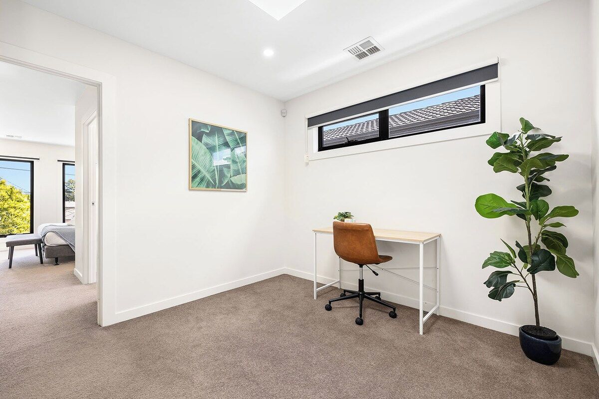A room with a desk, chair, potted plant, and a window with blinds.