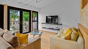 A living room with a sofa, a coffee table, and a TV mounted on the wall. - Mercia House - sleeps 8 guests  in 4 bedrooms (Cheltenham)