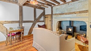 A cozy room with exposed wooden beams, a fireplace, a chessboard, and a plush sofa. - Mercia House - sleeps 8 guests  in 4 bedrooms (Cheltenham)