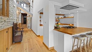 A modern kitchen with a wooden island, bar stools, and a stone wall. - Mercia House - sleeps 8 guests  in 4 bedrooms (Cheltenham)