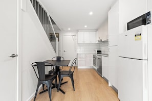A compact kitchen with white cabinets, a black dining table, and chairs.