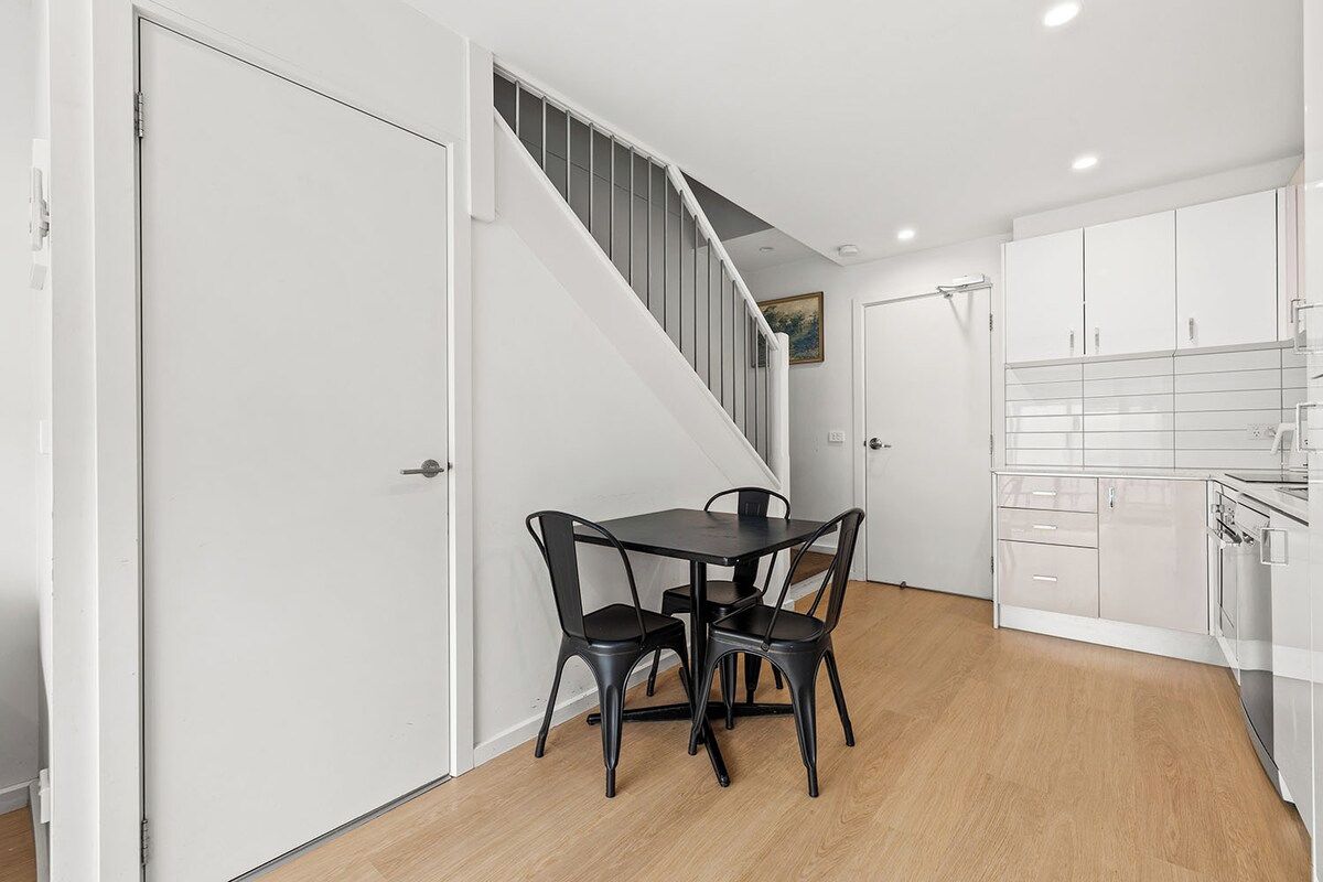 A modern kitchen with white cabinets, a black dining table with chairs, and a staircase leading to an upper level.