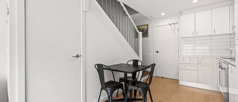A modern kitchen with white cabinets, a black dining table with chairs, and a staircase leading to an upper level.