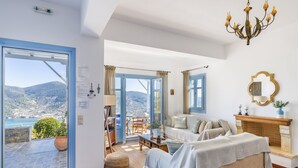 A spacious living room with a large window, a fireplace, and a view of the mountains. - Villa Avaton Magnificent sea view and Skopelos town (Skopelos)