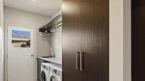 A laundry area with a washing machine, a dryer, and a wooden door with a handle. - Luxurious Home Close to The Beach (Surf Beach)