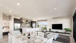 A modern living room with a dining area, a kitchen, and a TV. - Luxurious Home Close to The Beach (Surf Beach)