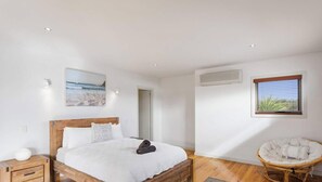 Een slaapkamer met een houten bed, een nachtkastje, een stoel, een raam met jaloezieën en een airconditioner.
