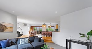 A modern living room with a grey sofa, a wooden coffee table, and a dining area with wooden chairs.