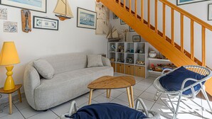 Ein gemütliches Wohnzimmer mit einer Couch, einem kleinen Holztisch, einem Korbstuhl und einer Treppe mit Holzbalkonen.