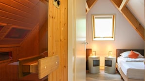 Une chambre mansardée chaleureuse, avec un plafond en pente, un banc en bois, un lit avec des oreillers et deux lampes de chevet.