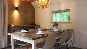 Un coin repas avec une table en bois, des chaises, une plante en pot et une fenêtre donnant sur un paysage verdoyant.