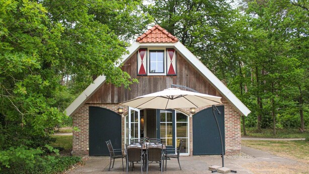 Un bâtiment rustique en bois, avec une façade en briques, un toit en tuiles et un patio couvert comprenant une table et des chaises.