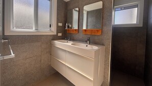 Ein modernes Badezimmer mit zwei Waschbecken, einem großen Spiegel und einem Fenster für natürliches Licht.
