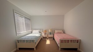 Ein Schlafzimmer mit zwei Einzelbetten, einem Fenster mit Jalousien, einem Nachttisch mit Lampe und einem Teppichboden.