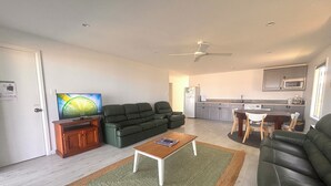 Ein modernes Wohnzimmer mit einer Couch, einem Couchtisch und einem Fernseher. Es gibt eine Küchenzeile mit einem Esstisch und Stühlen.