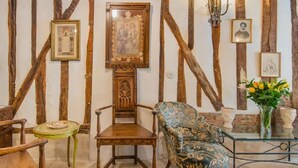 A room with exposed wooden beams, a wooden chair, a table with a vase of flowers, and framed pictures on the wall. - Romantic, air-conditioned apartment in Paris in the heart of the historic Marais district (Paris)