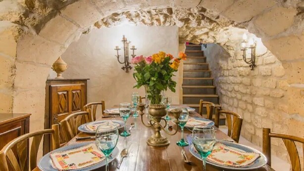 A dining area with a wooden table set for six, surrounded by stone walls and a staircase. - Romantic, air-conditioned apartment in Paris in the heart of the historic Marais district (Paris)