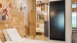 A bedroom with a stone wall, a bed with white bedding, a wooden door, and a black wardrobe. - Romantic, air-conditioned apartment in Paris in the heart of the historic Marais district (Paris)